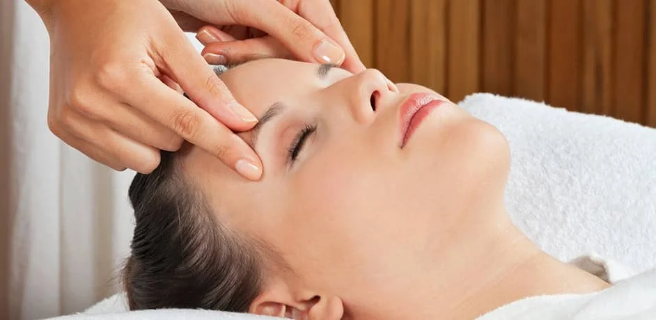 Therapist gently massaging a woman’s forehead and temples during a facial therapy treatment.